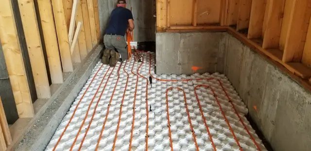A close-up view of radiant floor heating tubing laid out on a bed of insulation material. The orange