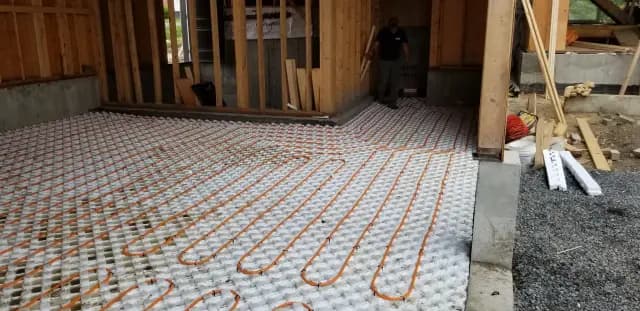 A close-up view of orange radiant floor heating tubing laid out on a white insulation mat. The tubing