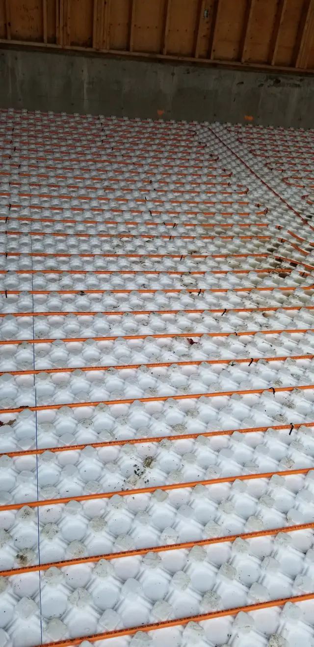 A close-up view of a radiant floor heating system with orange tubes embedded in a white insulation mat.
