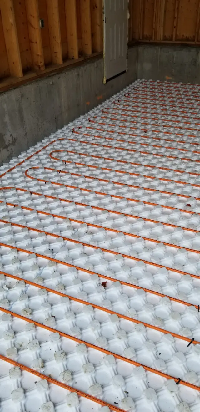 Radiant floor heating system with orange tubing on a white insulation mat