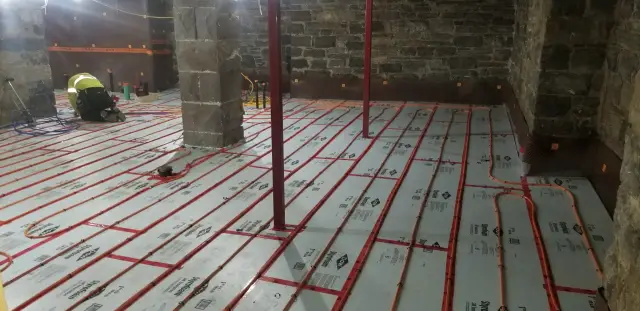 A close-up view of the radiant floor heating system being installed, showing the red tubing on a white