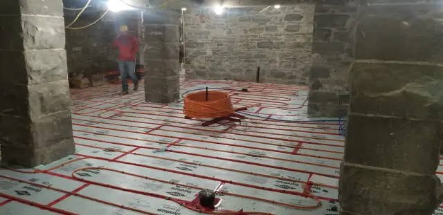 A close-up view of radiant floor heating tubing laid out on a white insulation mat. The tubing is