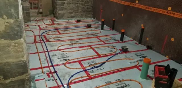 Tubing for radiant floor heating is laid out on a white insulation sheet with red markings and labels.