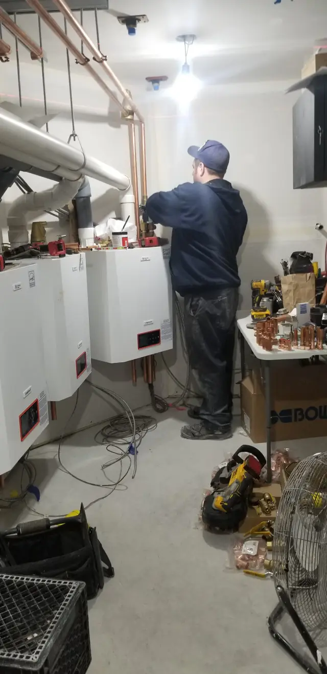 Copper pipes are neatly installed above a white water heater, with tools and materials scattered around the workspace