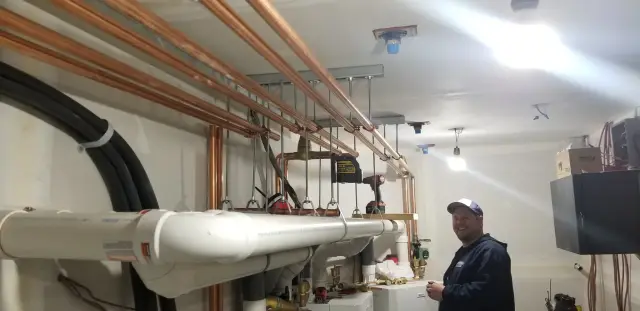 Copper pipes are installed in parallel on a white wall, with a in the background