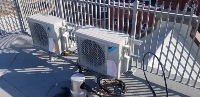 Outdoor Gree heat pump installed on a rooftop with a metal railing. The pump is white with a
