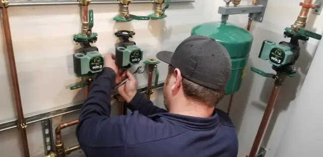 A is adjusting a valve on an HVAC system with a green expansion tank and multiple valves in