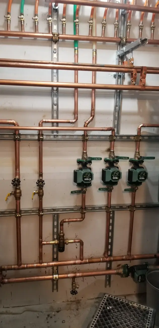 Copper pipes with green and orange hoses connected to various valves and fittings