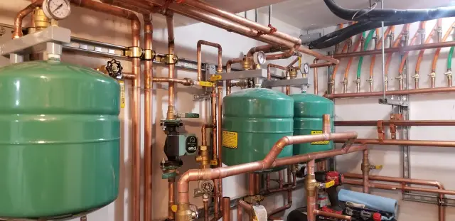 Copper pipes with green expansion tanks, valves, and fittings installed on a wall