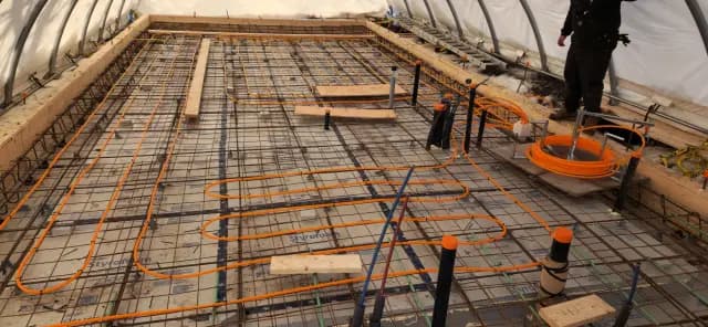 Radiant floor heating system with orange tubing and insulation layers installed on a construction site