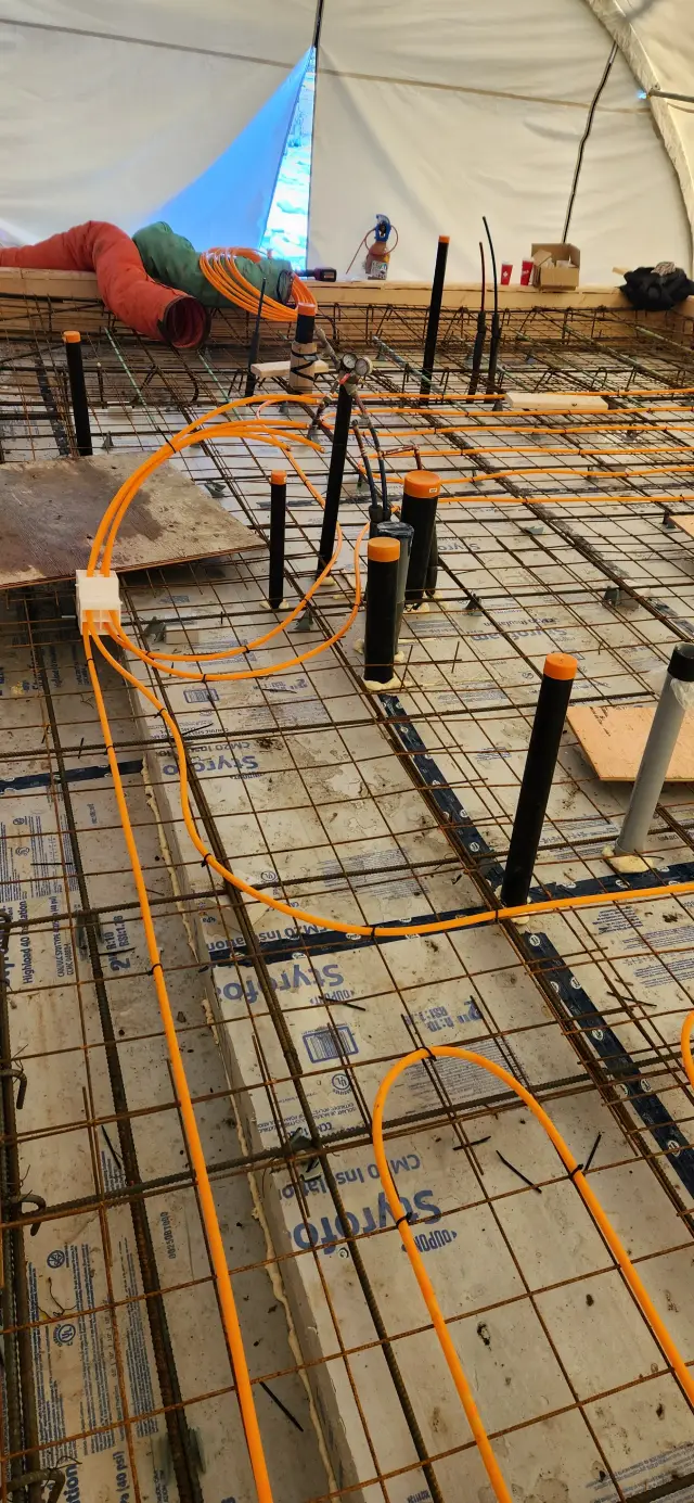 Orange tubing for radiant floor heating is laid out on a white insulation sheet with blue text detailing