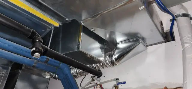 Metal ductwork with reflective surface, showing bends and connections, with a focus on the shiny, silver-colored metal