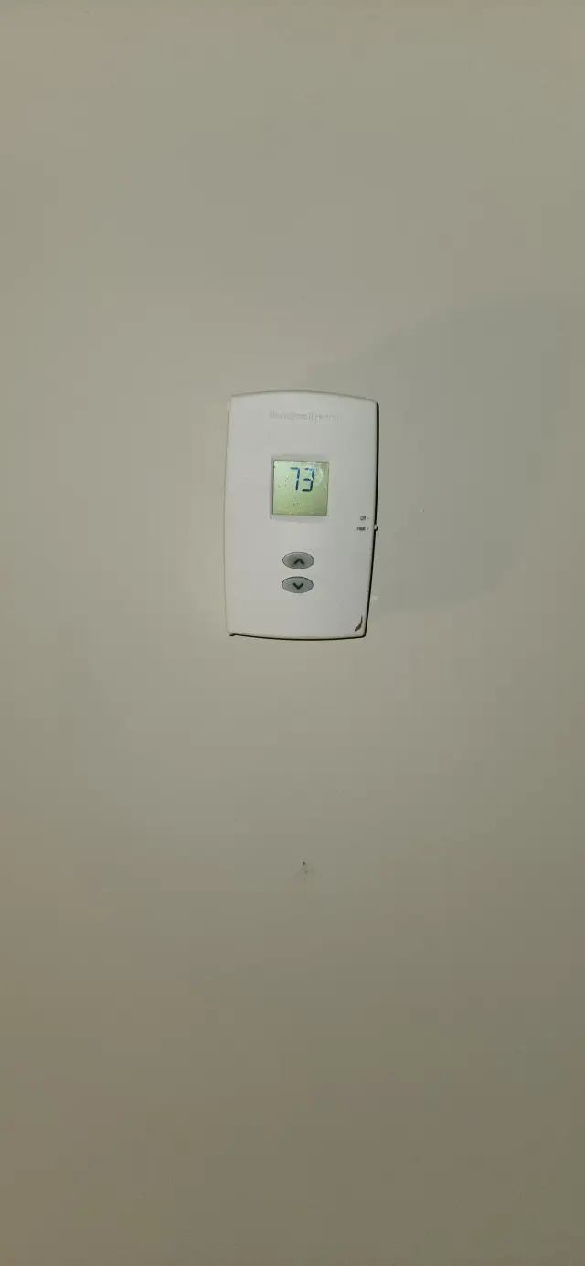 Thermostat with digital display showing 73 degrees, mounted on a beige wall