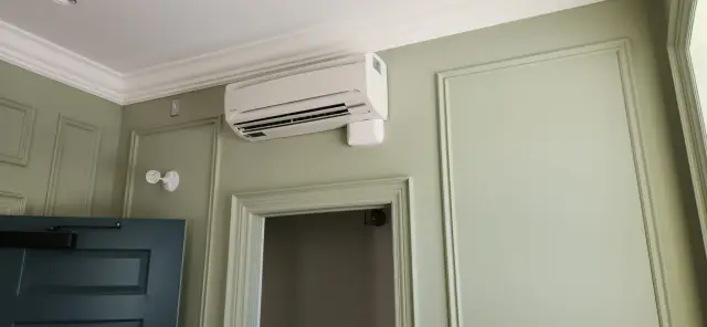 Air conditioning unit with a white casing is mounted on a wall with a green paint finish