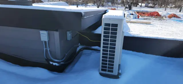 Outdoor Gree heat pump installed on roof with snow around