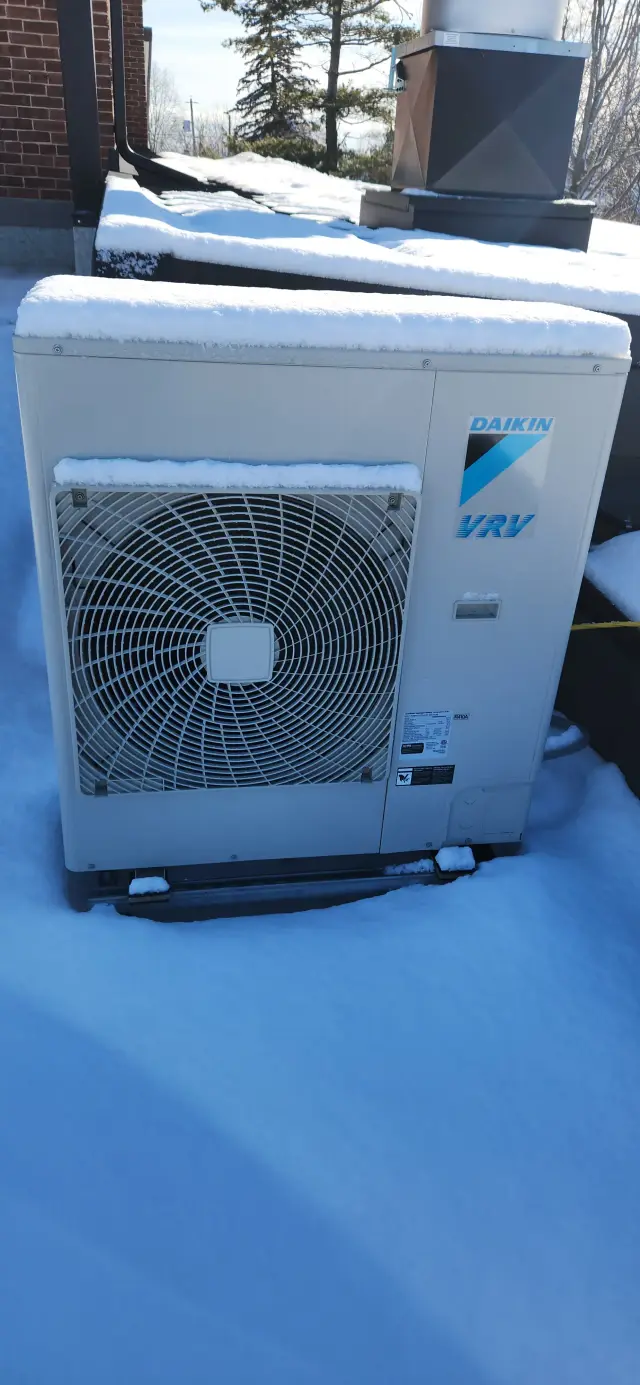 A Daikin VRF heat pump is installed outdoors, covered with a light layer of snow. The unit is