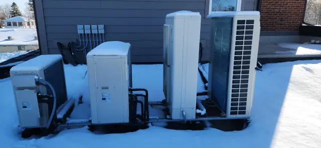 A technician is inspecting an HVAC unit, with snow on the ground and roof, highlighting the importance of regular maintenance during winter months.