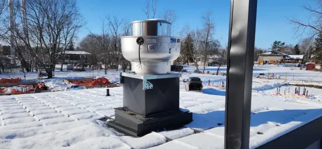 A technician inspects an HVAC unit on a snow-covered rooftop, emphasizing the significance of winter maintenance for efficient heating systems.