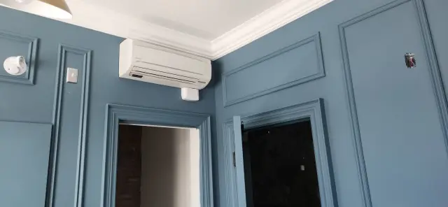 A technician is installing an air conditioning unit into a blue wall, highlighting the significance of routine service for optimal indoor climate control.