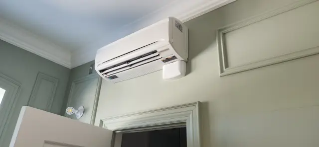 Air conditioning unit mounted on a wall with a white casing and a control panel visible