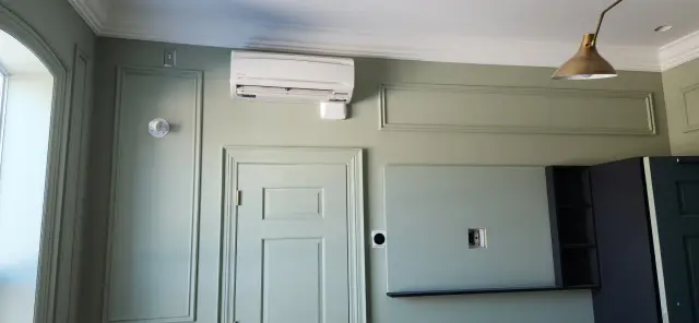 A technician is meticulously fitting an air conditioning unit into a wall, with a focus on precision and safety.