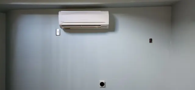 Air conditioning unit mounted on a wall with a white casing and a vent at the bottom