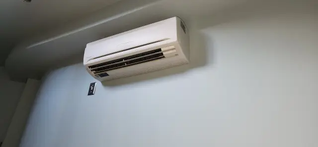 A technician is fitting an air conditioning unit into a wall, highlighting the importance of professional installation for optimal efficiency and safety.