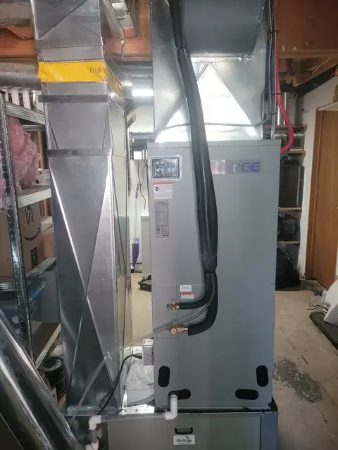 Outdoor Gree heat pump with silver casing, black wiring, and a digital display. Installed in a residential setting