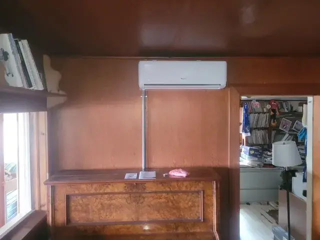 A technician is in the process of mounting an air conditioning unit onto a wooden wall, with a focus on the equipment and the installation process.