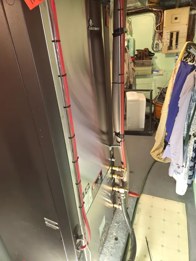 Outdoor Gree heat pump installed on concrete slab with metal framework. Red and black wiring connected to the