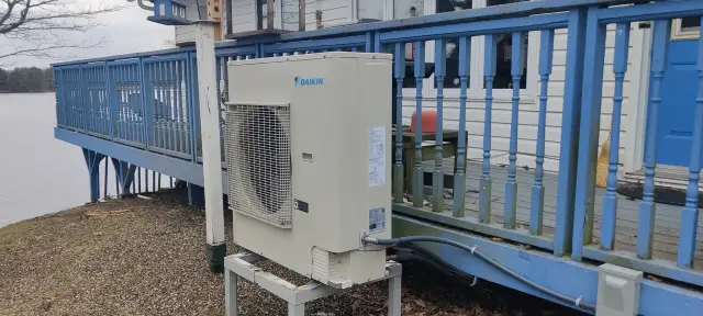A technician is examining an outdoor HVAC unit on a deck, with a focus on the equipment's components, indicative of routine maintenance or inspection.