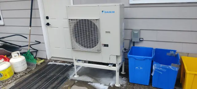 A technician is examining a large white HVAC unit outside a house, with a focus on its components, indicative of a maintenance check.