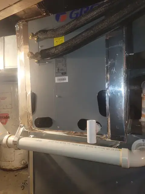 A technician's hands are carefully positioned on a metal part of an HVAC unit, with a focus on precision and safety. The setting suggests an indoor environment…