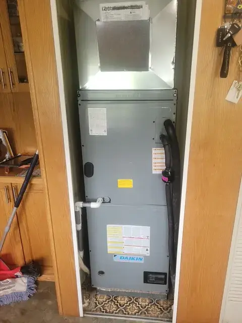 A Daikin air conditioning unit is installed vertically in a narrow space between wooden walls, with a vent