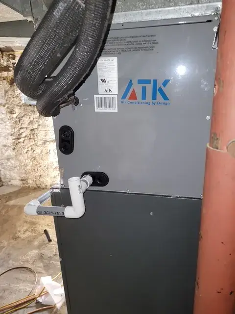 A close-up of the ATK Air Conditioning unit installed in a basement, showing the brand logo and a