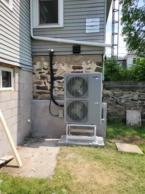 A large, gray outdoor heat pump with two fans is installed on a concrete pad next to a