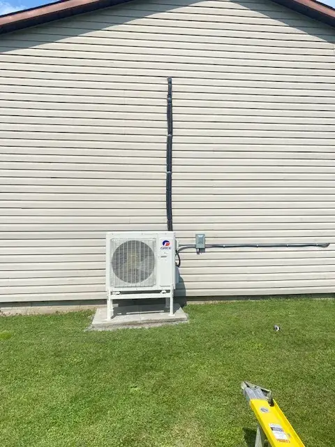 Outdoor Gree heat pump with a large fan and a long black exhaust tube, installed on a concrete