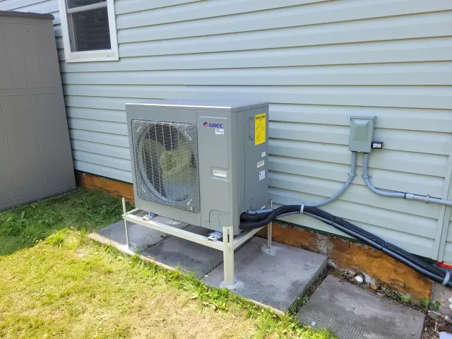 A newly installed outdoor Gree heat pump with a large fan and a gray casing is placed on