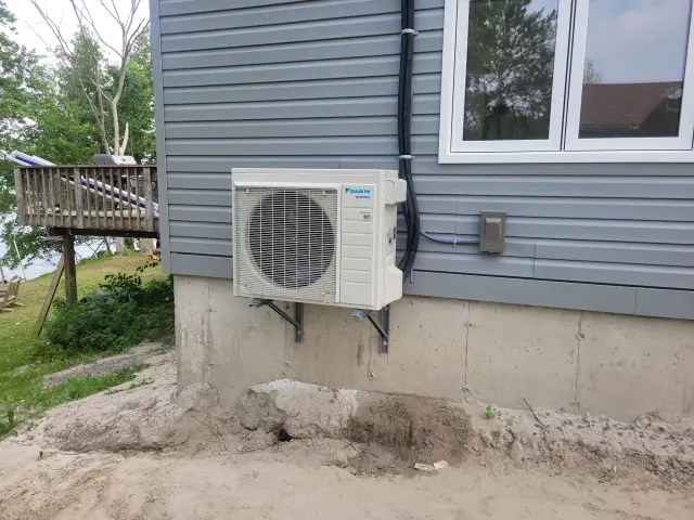 A new outdoor heat pump unit is installed on the side of a house, with a large fan