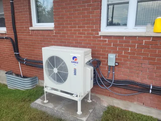 A newly installed outdoor Gree heat pump with a large fan and black wiring connected to the building.
