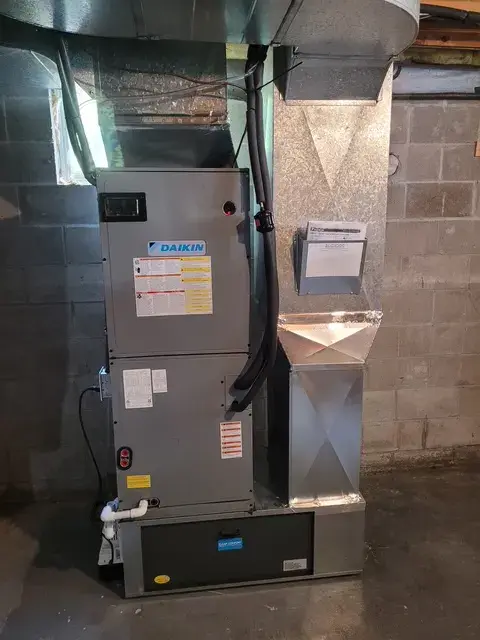 A Daikin air conditioning unit is installed in a basement with ductwork and wiring visible. The unit is