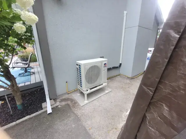 A new outdoor Gree heat pump is installed on the side of a house, with a patio and