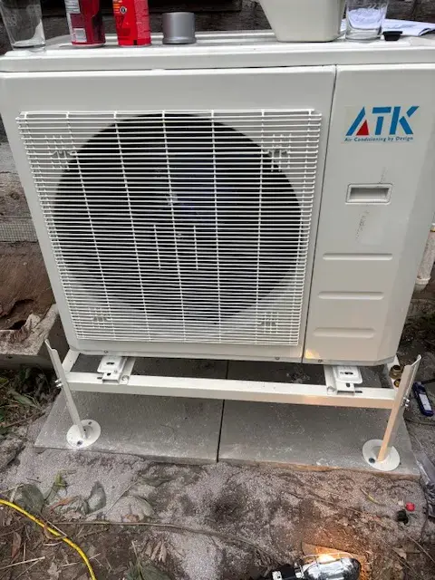 A newly installed outdoor Gree heat pump with a large fan and a white casing is placed on