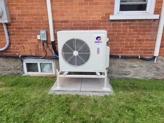 A new Gree heat pump is installed outside a brick house, with a large fan visible and electrical