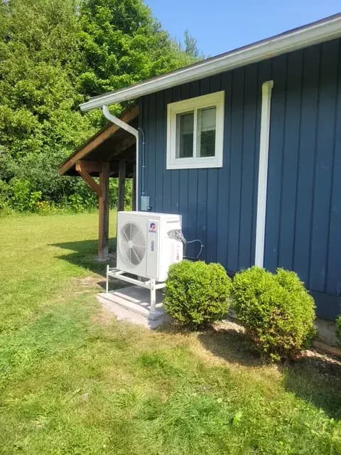 A Gree heat pump unit is installed outside a house. It's a white, rectangular unit with a large