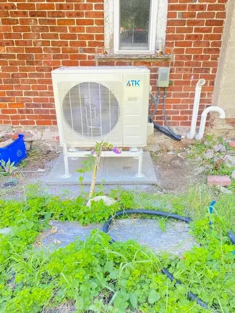 A newly installed outdoor Gree heat pump with a large fan and a white casing is placed on