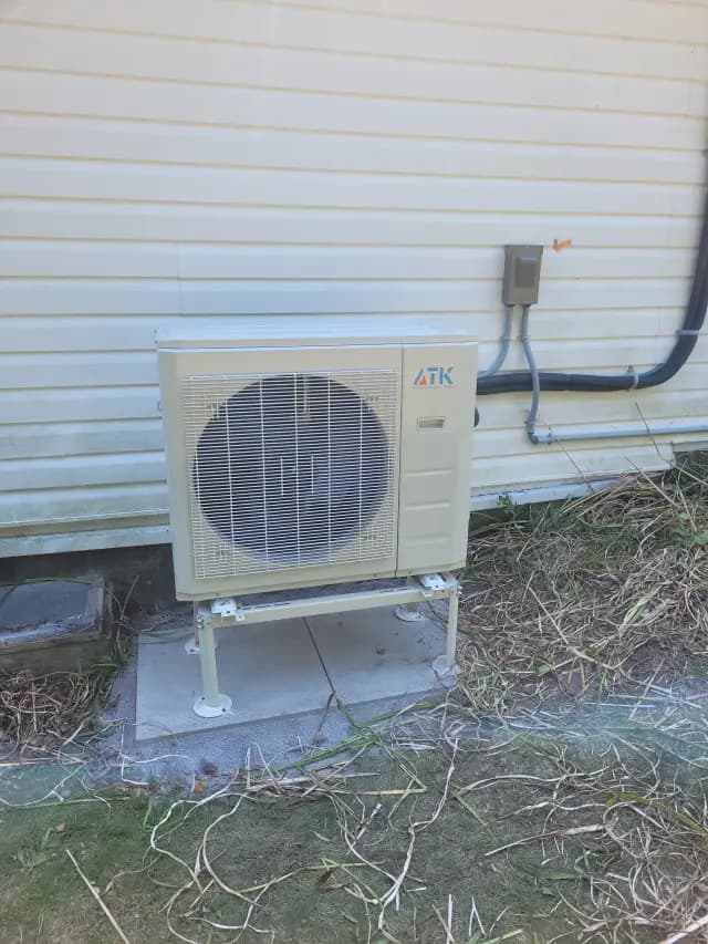 A newly installed outdoor Gree heat pump with a large fan and a beige casing is placed on