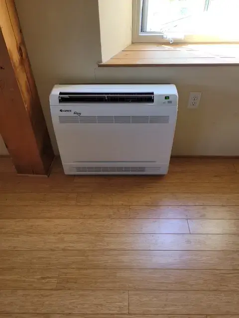 A new outdoor Gree heat pump is installed on the concrete foundation of a house. The pump is