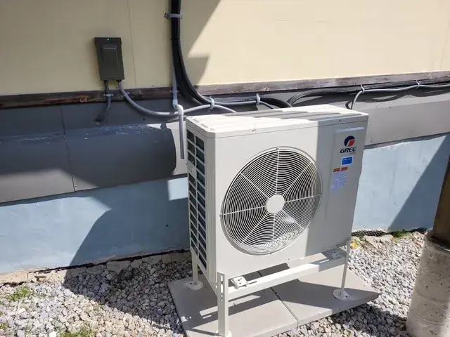 A large outdoor unit with a circular fan is installed on a platform surrounded by gravel. The unit