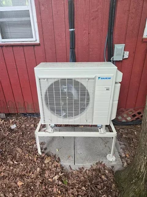 Outdoor unit of a Gree heat pump with a large fan, installed on a platform with a red